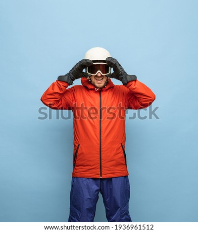 Active lifestyle. Young athletic man in bright red and blue ski suit, helmet and goggles posing isolated on blue background. Concept of human emotions, sport and healthy life. Copy space for ad.