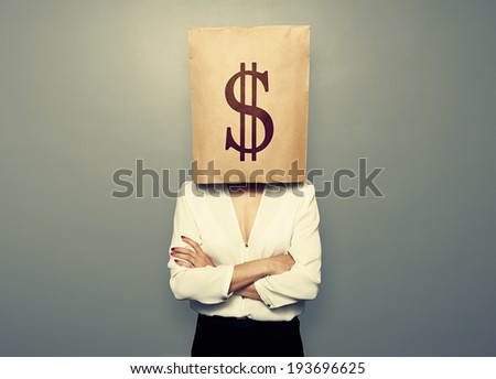businesswoman hiding under paper bag with dollar sign over dark background