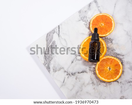 Vitamin C serum, organic orange essential oil bottle with dropper on white marble background with orange slices. Natural skin care concept, flat lay
