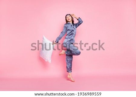 Full length body size photo of girl wearing nightwear keeping pillow jumping looking blank space isolated on pastel pink color background Royalty-Free Stock Photo #1936989559