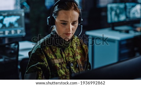 Beautiful Female Military Surveillance Officer in Headset Working in Central Office Hub for Cyber Operations, Control and Monitoring for Managing National Security, Technology and Army Communications. Royalty-Free Stock Photo #1936992862