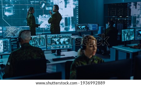Military Surveillance Team of Officers Locked a Target on a Vehicle from a Satellite and Monitor it on a Big Display in Office for Cyber Operations for Managing Security and Army Communications. Royalty-Free Stock Photo #1936992889