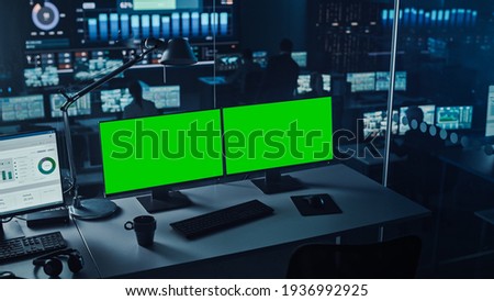 Two Digital Computer Screens with a Green Mock Up Chromakey in Modern Monitoring Office. Control Room with Specialists and Managers Sit in Front of Computers.