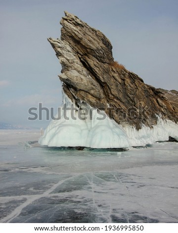 Dramatic graphical gray rock sharp texture white coastal splash ice Ogoy island Baikal lake Russia. Snow field landscape. Winter clouds overcast Visited popular innocent Tourism journey.  Royalty-Free Stock Photo #1936995850