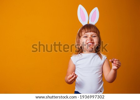 Little blond girl with dirty chocolate bunny ears eating Easter egg Royalty-Free Stock Photo #1936997302