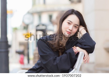 Portrait Asian beautiful woman in dark blue long sleeve shirt sits on chair in park outdoor.
