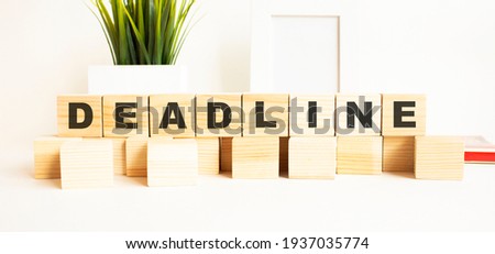 Wooden cubes with letters on a white table. The word is DEADLINE. White background with photo frame, house plant.