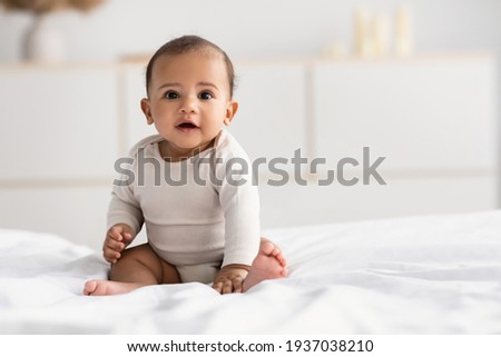 Cute little African American infant sitting on bed Royalty-Free Stock Photo #1937038210