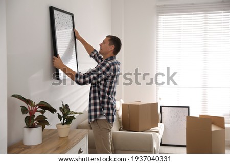 Man hanging picture on white wall in room. Interior design