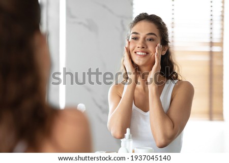 Woman Touching Smooth Face Skin Looking In Mirror In Bathroom Royalty-Free Stock Photo #1937045140