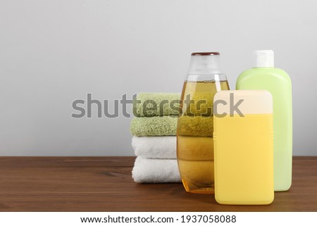 Different shower gel bottles with towels on wooden table. Space for text