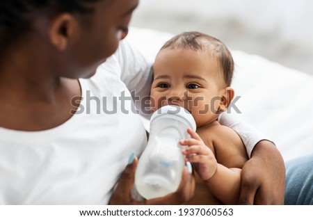 African American woman feeding her child from baby bottle Royalty-Free Stock Photo #1937060563