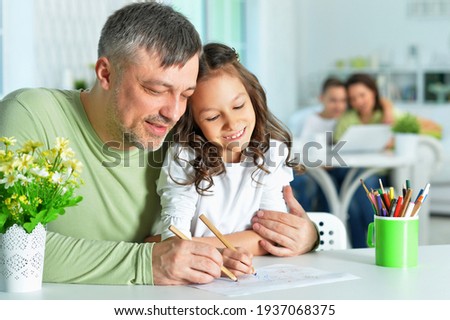 Portrait of happy father and his cute daughter drawing together at home