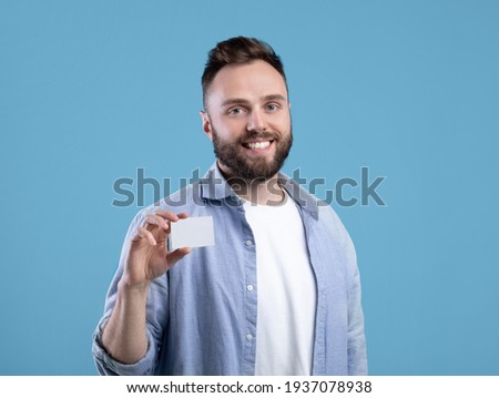 Happy young man showing empty business card with space for design over blue studio background