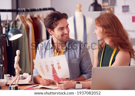 Male And Female Students Or Business Owners Working On Designs In Fashion Studio Together
