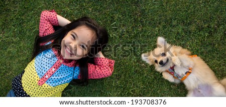 Happy Asian girl with her doggy portrait lying on lawn together. Royalty-Free Stock Photo #193708376
