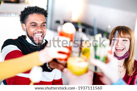 Young friends drinking at cocktail bar wearing open face mask - New normal friendship concept with couple having fun together toasting drinks at restaurant - Bright filter with focus on left guy