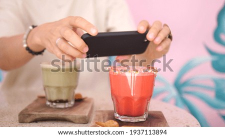 Hands taking a picture of pink smoothie decorated with sprinkles and an Ice coffee served on the wooden trays