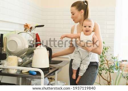 Young mother with a baby in her arms in the kitchen. Mom washes the baby's pacifier. The difficulties and joys of motherhood. High quality photo