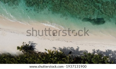 Aerial picture of one man lying on sandy beach with tropical trees, palm, white sand and turquoise water. Single person relaxing on picturesque island. Breathtaking scenery. Vacation location.