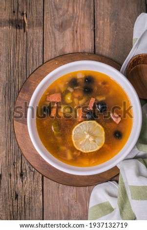 Slavic Solyanka soup in a white bowl on dark wooden background with copy space. Top view. Famous traditional Ukrainian and Russian saltwort soup with lemon.