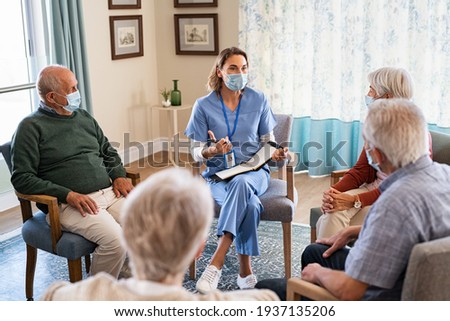 Group of senior people listening to nurse wearing face mask. Counselor wearing surgical mask talking to group of old people. Psychological support for elderly and lonely people in a community centre. Royalty-Free Stock Photo #1937135206