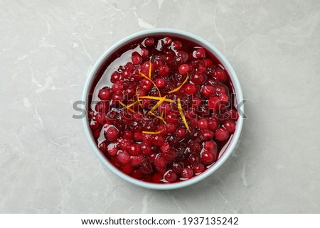 Fresh cranberry sauce with orange peel on light marble table, top view