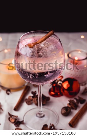 Coctel de ginebra rosa con canela, sobre un mantel blanco decorado con trozos de piñas y madera, con dos velas aromaticas