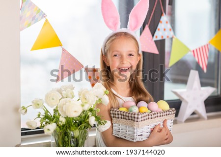 Pretty little girl wearing bunny ears and holding basket with easter eggs at home during coronavirus covid-19 outbreak. 