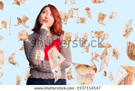 Young beautiful redhead woman wearing casual heart sweater serious face thinking about question with hand on chin, thoughtful about confusing idea
