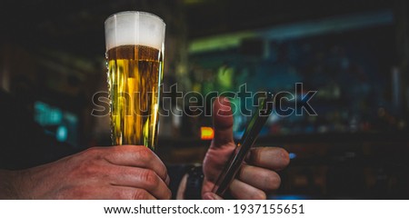 close up of man hand hold smartphone, drinking beer and reading message at bar or pub