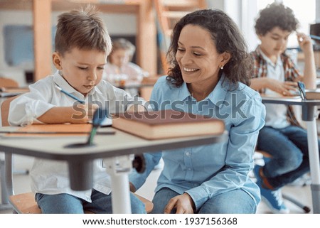 Happy kind teacher is helping a boy in elementary school lessons Royalty-Free Stock Photo #1937156368