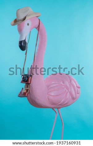 Figure of a pink flamingo tourist in a straw hat holding a camera