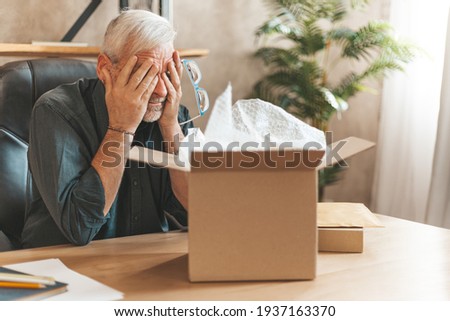 Damaged parcel box. Upset mature man closes his eyes, returns the goods to the store. A disgruntled online shopper. Broken item, delivery problem. Royalty-Free Stock Photo #1937163370