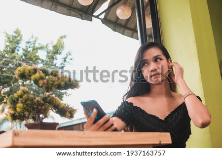 An asian teenager puts on some bluetooth earphones to listen to music or a podcast while waiting for her boyfriend or other meeting.