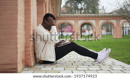 Young black man working remotely with laptop outside. African entrepreneur or student typing on computer