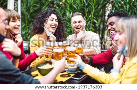 Multicultural people toasting beer wearing open face mask - New normal life style concept with friends having fun together at brewery bar garden - Warm filter with focus on woman in yellow clothes Royalty-Free Stock Photo #1937176303