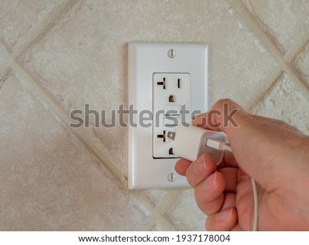 Plugging in electrical usb cord and charger plug in wall outlet. Cell phone power adapter brick and cord in GFCI wall plug. Royalty-Free Stock Photo #1937178004