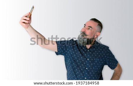 40-45 year old Caucasian hipster with a gray beard using his cell phone to take a self-portrait with an interesting and confident face
