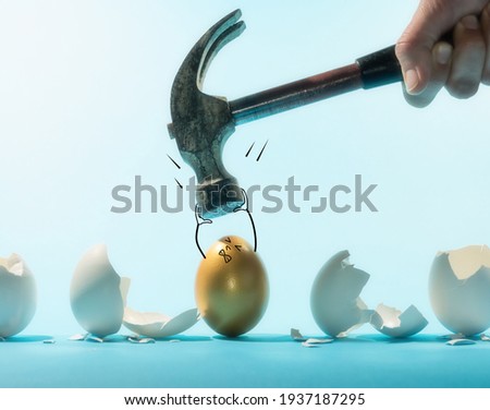 Intact golden egg holds the hammer among broken white eggs. Funny character. The concept of reliability, resistance to adverse conditions. Royalty-Free Stock Photo #1937187295