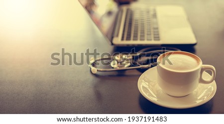 Coffee placed on the desk beside the computer, laptop and Earpiece.