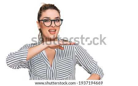 Young caucasian woman wearing business shirt and glasses gesturing with hands showing big and large size sign, measure symbol. smiling looking at the camera. measuring concept. 