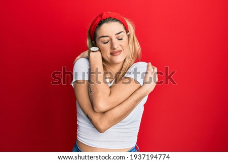 Young caucasian woman wearing casual white t shirt hugging oneself happy and positive, smiling confident. self love and self care 