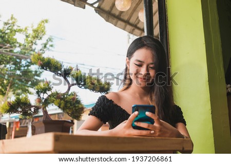A happy young asian lady busily texting or chatting on the phone. At an al fresco cafe. Royalty-Free Stock Photo #1937206861