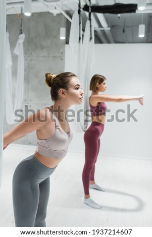 pretty young sportswomen warming up near fly yoga hammocks, blurred background