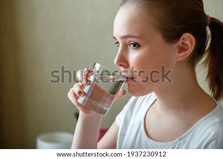 Young woman drinks glass of pure water in morning after waking up. Happy teen girl maintains water balance for body health by drinking a transparent cup of clean water Royalty-Free Stock Photo #1937230912
