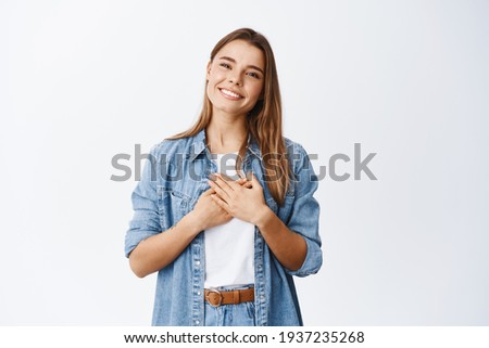 Portrait of touched young woman feeling flattered, holding hands on heart and smiling white teeth, say thank you, appreciate help, being grateful for nice gesture, white background Royalty-Free Stock Photo #1937235268