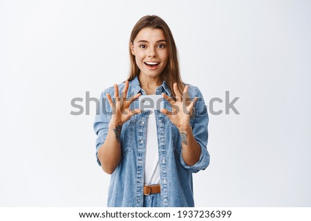 Portrait of smiling and surprised young woman holding plastic credit card in hands over chest, advertising new banking feature, recommending bank, white background
