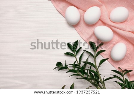 White eggs on a pink tablecloth. Tabletop texture. Green leaves. Easter plot.