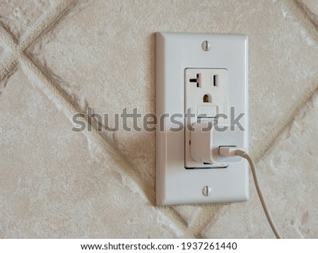 USB cell phone power adapter brick and cord in GFCI wall plug. Electrical cord and charger plug in wall outlet. Royalty-Free Stock Photo #1937261440